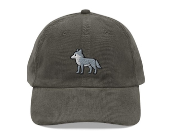 May include: A dark green corduroy baseball cap with a gray embroidered wolf design on the front. The cap has a curved brim and a fabric strap closure on the back.