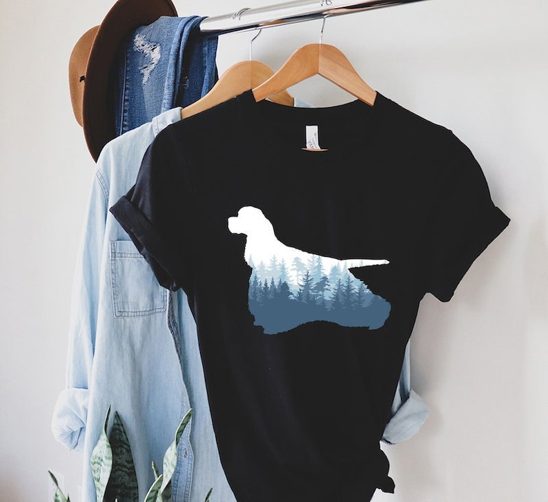 May include: Black t-shirt with a silhouette of a Cocker Spaniel dog with a blue and white forest design inside the silhouette.