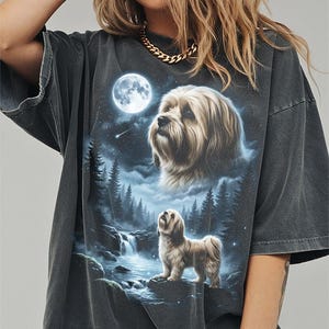 May include: Dark gray t-shirt featuring a detailed illustration of a dog under a full moon in a forest setting. The design includes a waterfall and a starry sky, creating a serene, nature-inspired scene. The shirt has a relaxed fit.