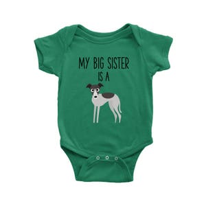 Puede incluir: Un body de bebé verde con el texto "Mi hermana mayor es una" y una imagen de dibujos animados de un galgo italiano gris y blanco.