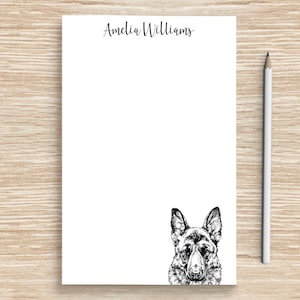 May include: White notepad with the name "Amelia Williams" printed at the top. A black and white illustration of a German Shepherd dog's head is at the bottom of the notepad.