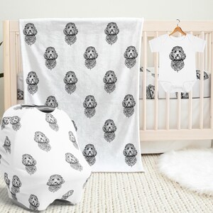 May include: A white baby blanket, car seat cover, and onesie with a black and white doodle of a dog's face repeated on the fabric.
