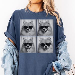 May include: Navy blue t-shirt featuring a four-panel image of a Pomeranian dog wearing sunglasses. The dog's expressions vary in each panel, with one showing its tongue out. The shirt is a comfortable, casual style.