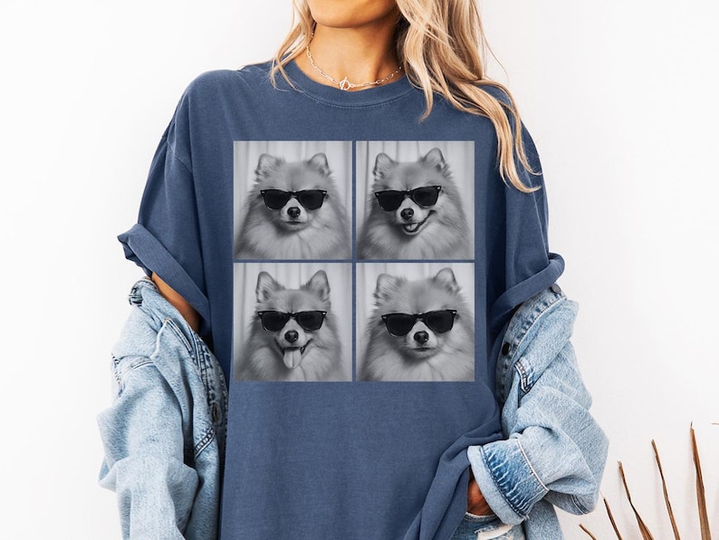 May include: Navy blue t-shirt featuring a four-panel image of a Pomeranian dog wearing sunglasses. The dog's expressions vary in each panel, with one showing its tongue out. The shirt is a comfortable, casual style.