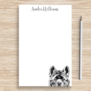 May include: White notepad with the name "Amelia Williams" printed at the top. A black and white illustration of a dog's head is peeking out from the bottom of the notepad.