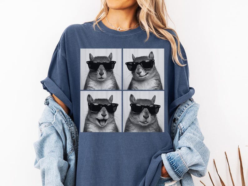 May include: A navy blue t-shirt featuring a four-panel image of a squirrel wearing black sunglasses. The squirrel's expressions vary in each panel, showcasing different moods. The shirt is a comfortable, casual style.