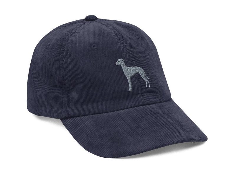 May include: A navy blue corduroy baseball cap with an embroidered grey silhouette of a dog on the front.