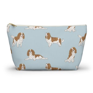 May include: A light blue zippered pouch with a repeating pattern of Cavalier King Charles Spaniels. The dogs are brown and white and are in various poses.
