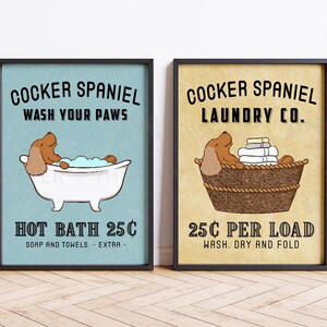 May include: Two framed prints with a cartoon cocker spaniel. The first print is blue and says "Cocker Spaniel Wash Your Paws Hot Bath 25c Soap and Towels - Extra". The second print is beige and says "Cocker Spaniel Laundry Co. 25c Per Load Wash. Dry and Fold".