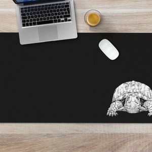 May include: Black desk mat with a white line drawing of a turtle on the right side.