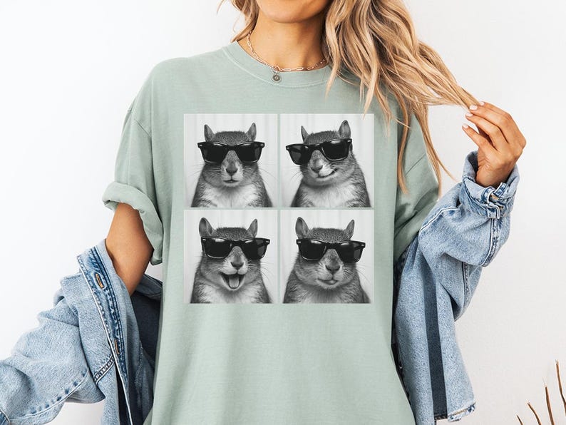 May include: A light green t-shirt featuring a four-panel image of a squirrel wearing sunglasses. The squirrel's expressions vary in each panel, with one showing a smile and another with its tongue out. The shirt is a comfortable, casual style.