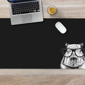 May include: Black desk mat with a white illustration of a capybara wearing glasses. The capybara is looking directly at the viewer.