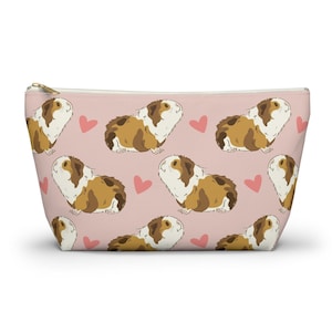 May include: A pink zippered pouch with a repeating pattern of brown and white guinea pigs and pink hearts.