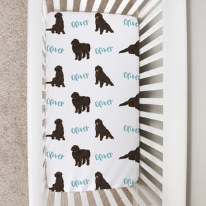 May include: White crib sheet with a repeating pattern of black dogs and the name "Oliver" in a teal script. The dogs are depicted in various poses. The sheet is inside a white crib.