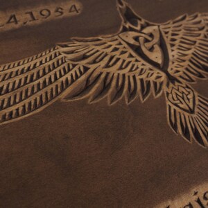 May include: A brown leather background with a carved design of a bird with outstretched wings. The date "9,24,1954" is carved at the top of the image. The word "geist" is partially visible at the bottom of the image.
