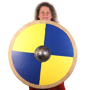Puede incluir: Un escudo redondo de madera con un borde de cuero y un jefe de metal en el centro. El escudo está pintado en cuatro secciones, alternando amarillo y azul.
