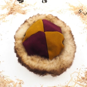 Può includere: Un cappello di lana bordeaux e oro con un ampio bordo di pelliccia marrone.