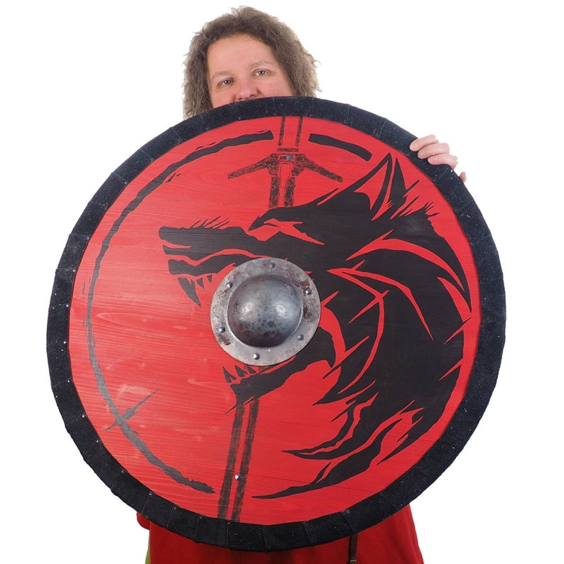 May include: A red wooden shield with a black wolf design and a metal center boss. The shield is held by a person.
