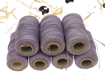 May include: A collection of lavender-colored thread spools. The spools are cylindrical, with the thread neatly wound around a cardboard core. The image is set against a white background with abstract, light brown and black shapes.
