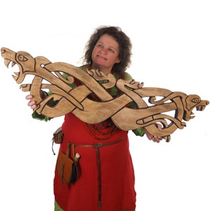 Peut inclure: Une femme tient une sculpture en bois de deux dragons entrelacés avec des détails complexes. La sculpture est de couleur brune avec des accents noirs et présente un motif de nœud celtique.
