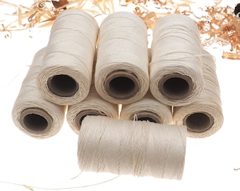 May include: A collection of off-white twine spools, each wound around a cardboard core. The spools are arranged in a cluster, with wood shavings in the background. The twine appears to be natural fiber, suitable for crafts or packaging.