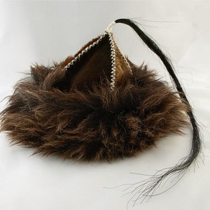 Può includere: Un cappello di pelliccia marrone con una lunga coda nera. Il cappello è in pelle e ha una cima appuntita. La pelliccia è spessa e soffice.