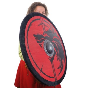 May include: A person holding a red and black shield with a black dragon design. The shield has a metal boss in the center.