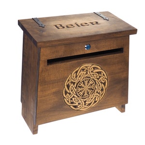 May include: A wooden mailbox with a hinged lid and a slot for mail. The mailbox is stained a dark brown color and features a decorative Celtic knot design on the front. The word "Beier" is carved into the lid.