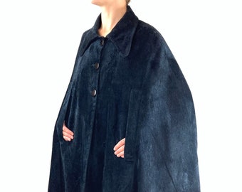 May include: A dark blue velvet cape with a collar and button closure. The cape has pockets on the sides and a long, flowing design.