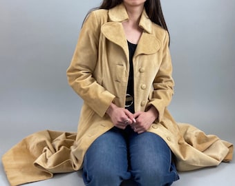 May include: A long, tan corduroy coat with a wide collar and a belt. The coat has a button closure and is worn by a person with blue jeans.