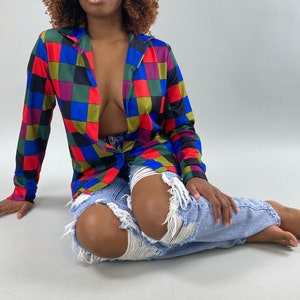 May include: A woman wearing a colorful checkered button-up shirt with a blue denim skirt. The shirt has a red, blue, green, and yellow checkered pattern.