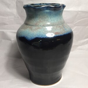 May include: A handcrafted ceramic vase with a dark blue base, transitioning to lighter blue and tan hues near the top. The vase has a ruffled rim and a glossy finish, suitable for displaying flowers or as a decorative piece.
