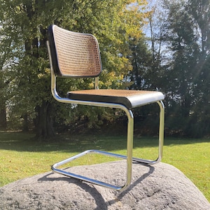 May include: A chrome and wicker chair with a black seat cushion. The chair is sitting on a large rock.