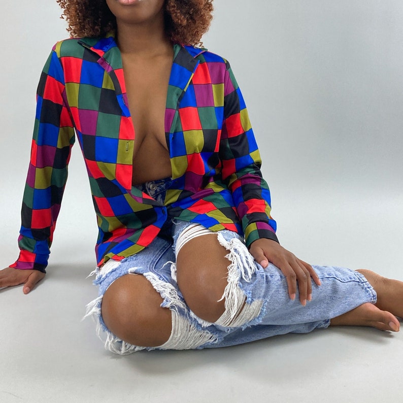 May include: A woman wearing a colorful checkered button-up shirt with a blue denim skirt. The shirt has a red, blue, green, and yellow checkered pattern.