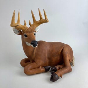 May include: A wooden sculpture of a brown deer lying down with its head turned to the side. The deer has large antlers with multiple points.