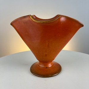 May include: A terracotta-colored ceramic vase with a wide, flared opening and a rounded base. The vase has a smooth, glossy finish.