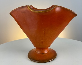 May include: A terracotta-colored ceramic vase with a wide, flared opening and a rounded base. The vase has a smooth, glossy finish.