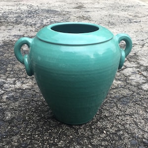 Könnte beinhalten: Ein großer, türkisfarbener Keramiktopf mit zwei Henkeln. Der Topf hat eine glatte, glasierte Oberfläche und eine abgerundete Form.