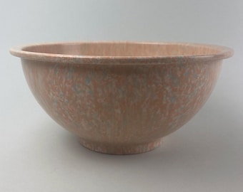 May include: A large, pink and white speckled mixing bowl made of plastic. The bowl has a rounded bottom and a wide, flat rim.