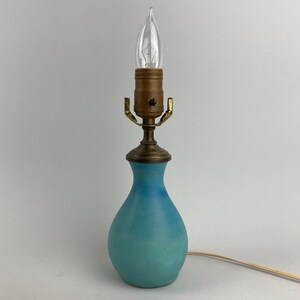 May include: A blue ceramic table lamp with a brass base and a clear light bulb.