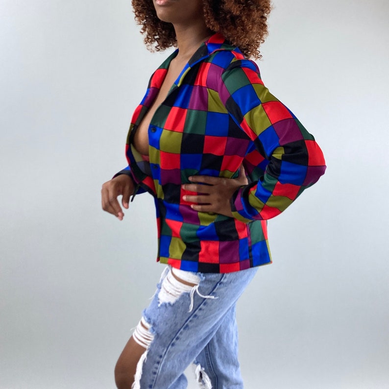 May include: A long-sleeved button-up shirt with a colorful checkered pattern in shades of red, blue, green, black, and purple. The shirt is made of a silky fabric and has a relaxed fit.