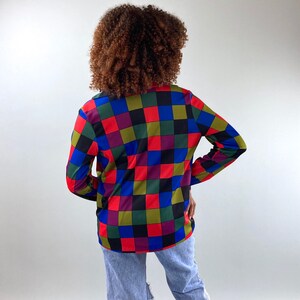 May include: A long-sleeved shirt with a checkered pattern in shades of red, blue, green, black, and purple.