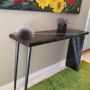 May include: A black console table with a live edge top and black metal legs. The table has a white resin finish and a decorative silver orb on top.
