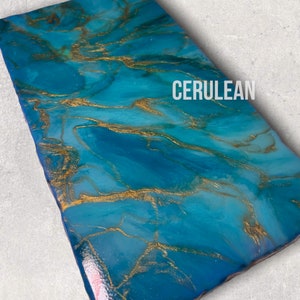 May include: A rectangular serving tray with a cerulean blue resin base and gold accents. The tray has a marbled effect with swirling patterns of gold and blue.