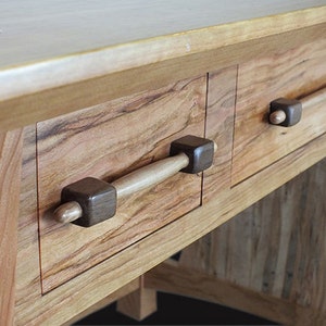 May include: A wooden desk with two drawers and wooden handles. The drawers are made of cherry wood with a natural finish. The handles are made of dark wood and have a simple design.