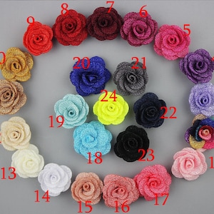 Puede incluir: Veinticuatro adornos de flores de tela de rosa en varios colores, incluidos rojo, rosa, azul, verde, amarillo y marrón. Las flores están dispuestas en un círculo sobre un fondo gris.