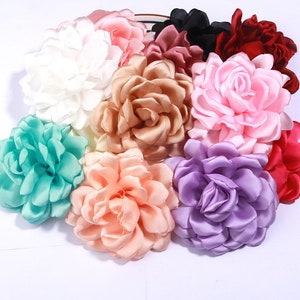 May include: Assortment of ten fabric flower embellishments in various colours, including white, beige, pink, purple, teal, and red. The flowers are made of satin and have a layered, ruffled design.