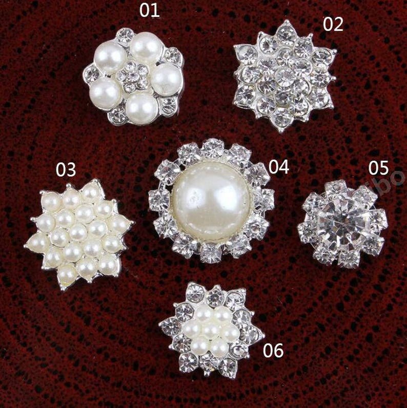May include: Six different silver-toned embellishments with pearl and rhinestone accents. The embellishments are arranged in a row on a brown surface. The embellishments are numbered 01 through 06.