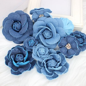 May include: A collection of blue denim fabric flowers. The flowers are in various sizes and shapes, with some having a more ruffled appearance than others.