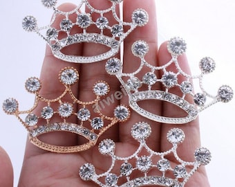 May include: Three silver and gold tone crown-shaped embellishments with clear rhinestones. The crowns are about 2 inches in diameter.